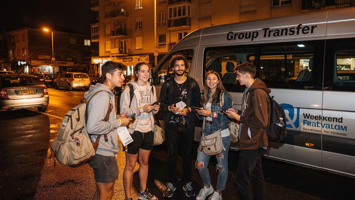 Young travelers with festival wristbands gathering beside a transfer van at night